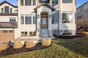 Entrance to property with stone siding, stucco siding, a garage, and a lawn
