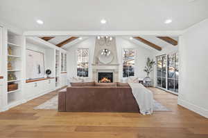 Living room featuring a chandelier, light wood-type flooring, beam ceiling, and a warm lit fireplace