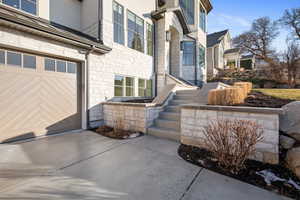 Entrance to property featuring stucco siding, stone siding, concrete driveway, and a garage