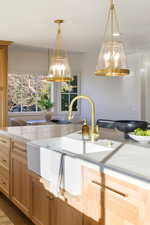 Kitchen featuring light wood finish cabinetry, decorative light fixtures, and light stone counters