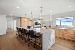 Kitchen with light wood finish cabinetry, a breakfast bar, light stone counters, light wood-type flooring, and a large island
