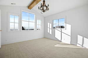 Spare room featuring a chandelier, light colored carpet, beamed ceiling, and healthy amount of natural light