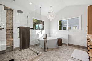 Bathroom with a wainscoted wall, tile walls, a freestanding bath, a stall shower, and vaulted ceiling