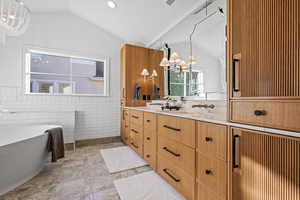 Bathroom featuring a chandelier, double vanity, wainscoting, vaulted ceiling, and tile walls