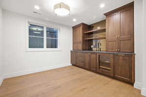 Indoor wet bar with open shelves, light wood-type flooring, dark countertops, dark wood finish cabinets, and recessed lighting