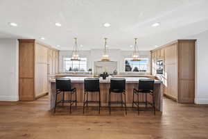 Kitchen with a breakfast bar area, a large island, light wood finished floors, hanging light fixtures, and light wood finish cabinetry