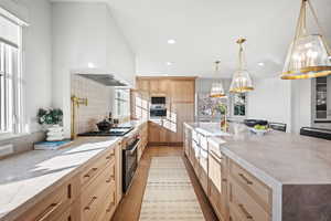 Kitchen with light wood finish cabinetry, stainless steel appliances, light stone counters, dark wood finished floors, and decorative light fixtures