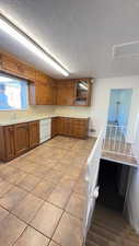 Kitchen featuring wood finish cabinets, light countertops, light tile patterned flooring, white dishwasher, and a textured ceiling