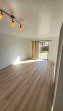 Empty room featuring light wood-style flooring, a textured ceiling, and rail lighting
