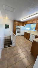Kitchen with wood finish cabinets, white appliances, light countertops, and dark tile patterned floors