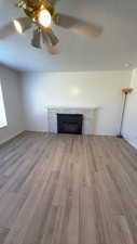 Unfurnished living room featuring light wood-style flooring, a tiled fireplace, ceiling fan, and a textured ceiling