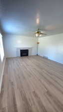 Unfurnished living room with a fireplace, light wood-type flooring, a textured ceiling, and ceiling fan