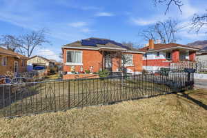 View of front of home featuring brick siding, roof mounted solar panels, and a fenced front yard
