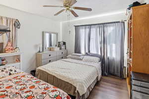 Bedroom with a textured wall, wood finished floors, and ceiling fan