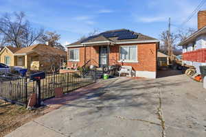 Bungalow-style house with roof mounted solar panels, brick siding, a fenced front yard, a shingled roof, and driveway