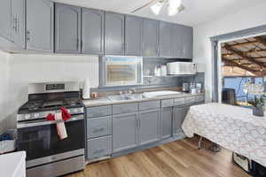 Kitchen featuring gray cabinetry, stainless steel range with gas cooktop, white microwave, light wood-type flooring, and ceiling fan
