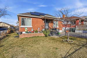 View of front of house featuring roof mounted solar panels, brick siding, and a chimney