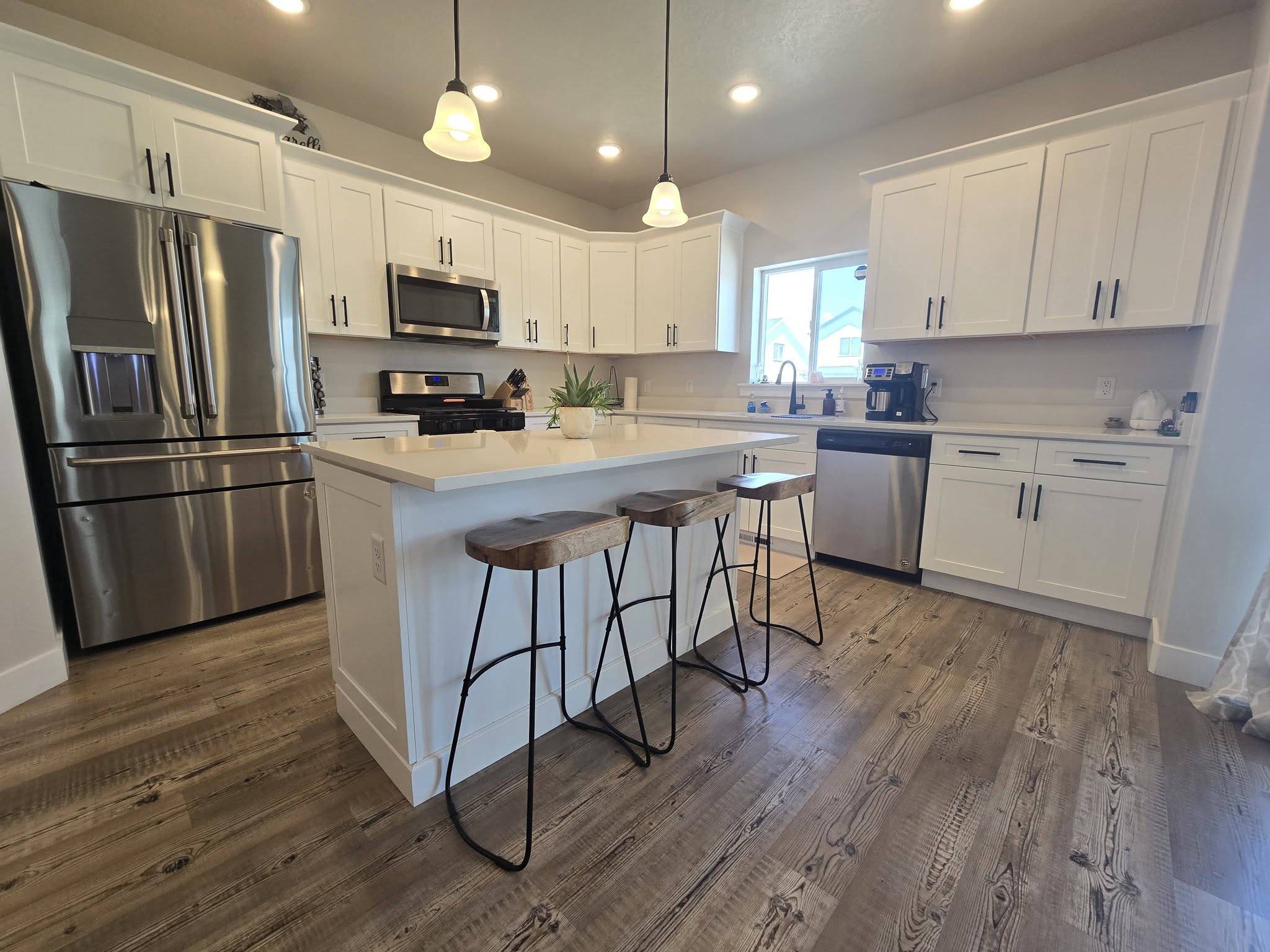 Kitchen featuring white cabinetry, stainless steel appliances, hanging light fixtures, and dark wood-style floors