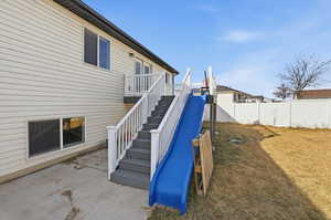 Back of house featuring stairs, a slide, and a patio area