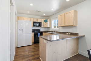 Kitchen with light wood finish cabinetry, black appliances, a peninsula, dark countertops, and dark wood-type flooring