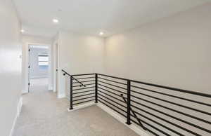 Hall with an upstairs landing, light colored carpet, and recessed lighting