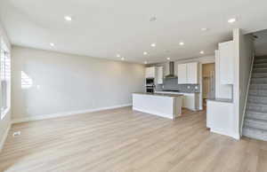 Kitchen with open floor plan, white cabinets, a kitchen island with sink, light wood finished floors, and recessed lighting