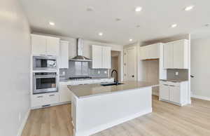 Kitchen with stainless steel appliances, white cabinetry, light wood-style floors, an island with sink, and recessed lighting