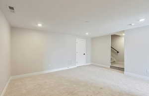 Finished basement with light colored carpet and recessed lighting