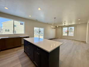 Kitchen featuring light wood-style flooring, open floor plan, light stone countertops, and a kitchen island