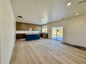 Kitchen with a kitchen island, light countertops, open floor plan, light wood-style flooring, and suspended lighting