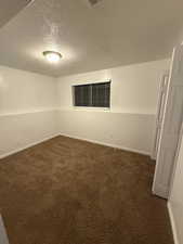 Unfurnished room with a textured ceiling and dark carpet