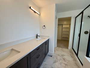 Bathroom with double vanity, a walk in closet, light marble finish flooring, and a shower stall