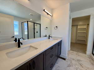 Bathroom featuring a spacious closet, a stall shower, light marble finish floors, and double vanity