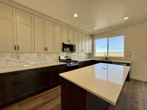 Two tone kitchen featuring stainless steel appliances, a center island, dark wood-style flooring, recessed lighting, and light stone countertops