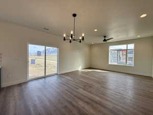 Spare room featuring hanging lights, dark wood-style flooring, healthy amount of natural light, and ceiling fan