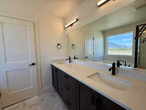 Bathroom with double vanity, light marble finish floors, and a bath