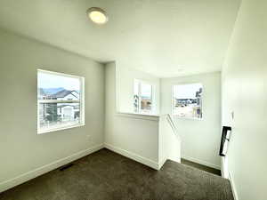 Spare room featuring healthy amount of natural light, dark carpet, and a textured ceiling