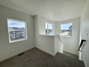 Unfurnished room featuring dark carpet and healthy amount of natural light