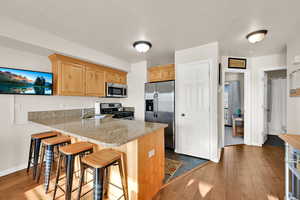 Kitchen with stainless steel appliances, dark wood-style flooring, a kitchen breakfast bar, a peninsula, and light stone countertops