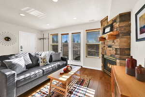 Living room with a stone fireplace, dark wood-type flooring, and recessed lighting