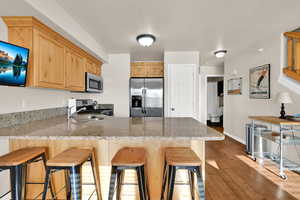 Kitchen with a peninsula, stainless steel appliances, light wood finish cabinets, dark wood-style flooring, and light stone counters