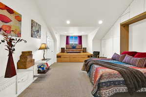 Versatile room featuring an elevated platform with integrated storage, sloped ceilings, recessed lighting, and soft carpet flooring