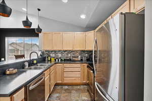 Kitchen featuring light wood finish cabinetry, stainless steel appliances, vaulted ceiling, decorative backsplash, and pendant lighting