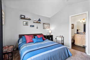 Bedroom featuring lofted ceiling, dark carpet, and ensuite bathroom