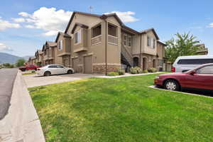 View of front facade with a front lawn, stone siding, stucco siding, and a garage