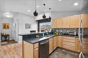 Kitchen featuring light wood finish cabinetry, stainless steel appliances, lofted ceiling, dark countertops, and a peninsula