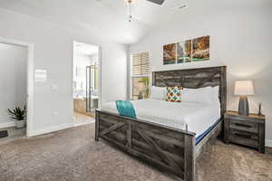 Bedroom with ensuite bath, light carpet, ceiling fan, and vaulted ceiling