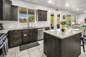 Kitchen with dark wood finish cabinets, stainless steel appliances, light stone counters, recessed lighting, and a center island