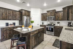 Kitchen featuring dark wood finish cabinetry, stainless steel appliances, a center island, light stone countertops, and recessed lighting