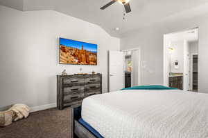 Bedroom featuring lofted ceiling, dark colored carpet, ensuite bathroom, and ceiling fan